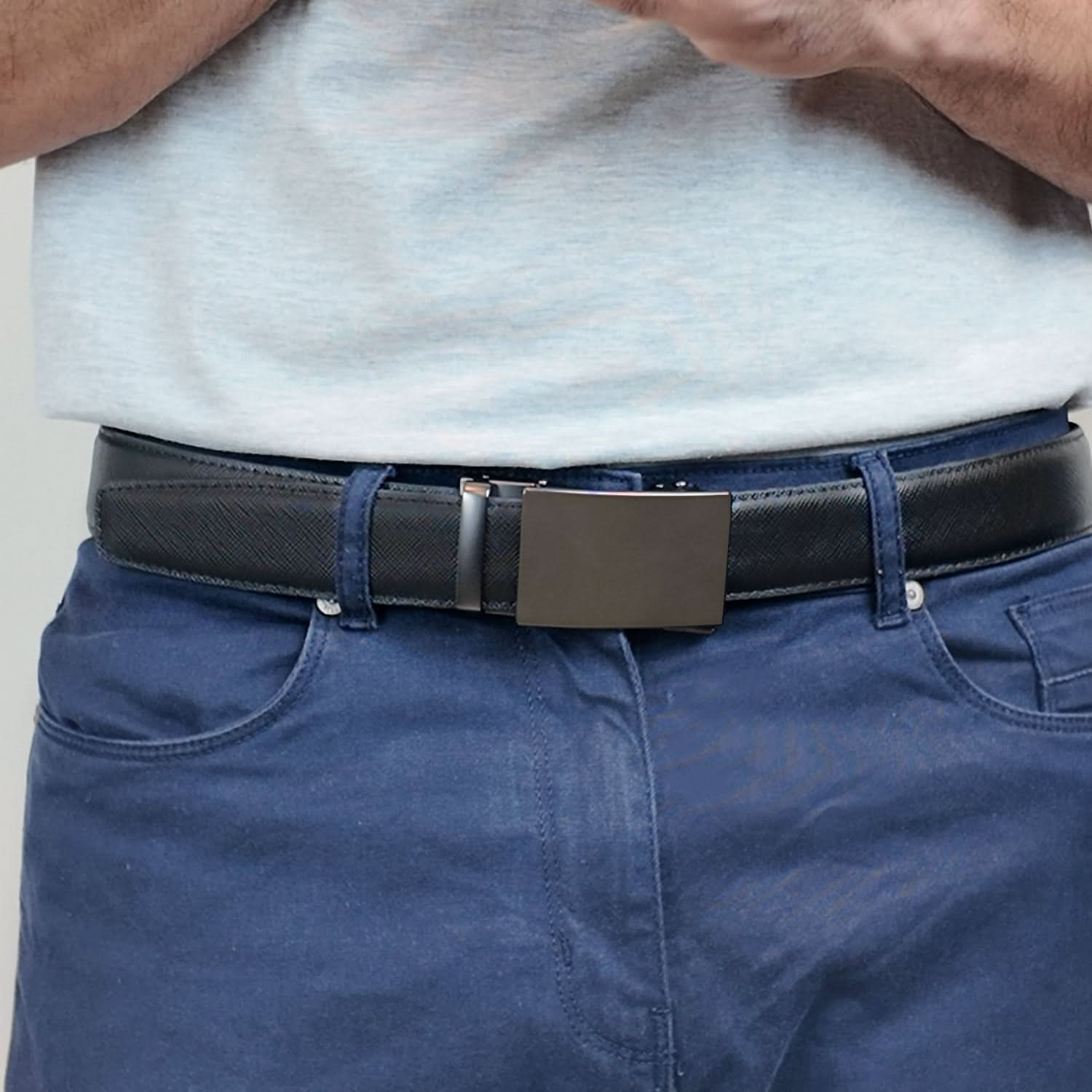 A man wearing a ratchet belt with a textured leather strap featuring line patterns and a rectangular gunmetal buckle, showcasing a modern, hole-free design for adjustable comfort.