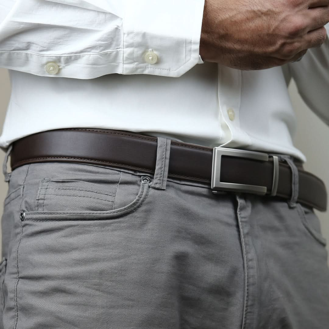 A man adjusting a modern seamless belt with no holes, featuring a smooth leather strap and a polished silver buckle.